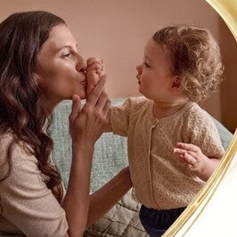 Foto di una mamma che bacia la mano di un bambino piccolo in un salotto caldo e accogliente.